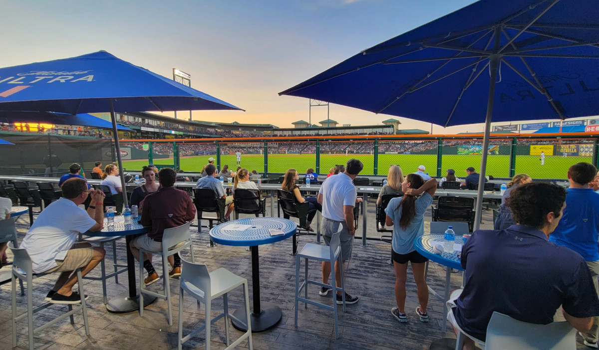 A patio of people talking at the edge of a baseball outfield