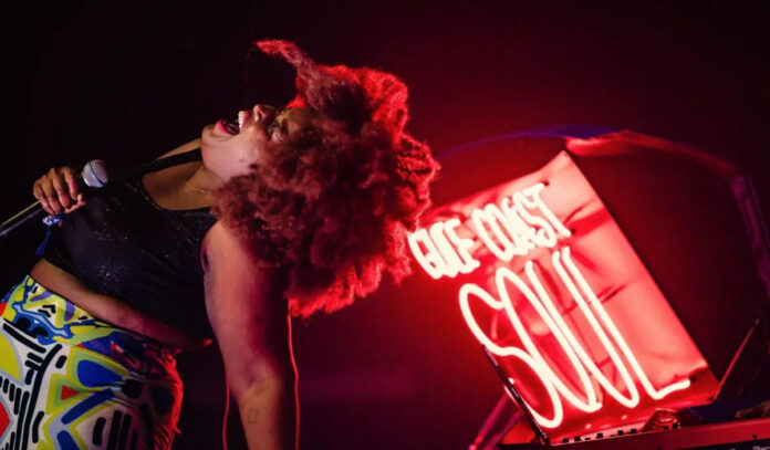 Kam Franklin of the Suffers sings with a neon sign behind her that says Gulf Coast Soul