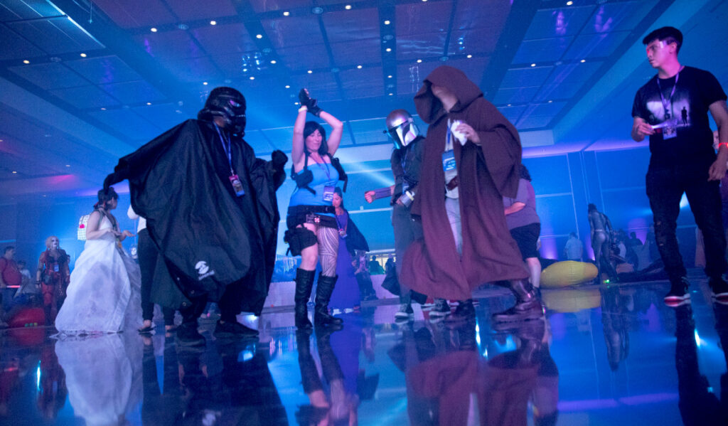 Fans cosplaying as Lara Croft and Star Wars characters dance in a blue-lit room