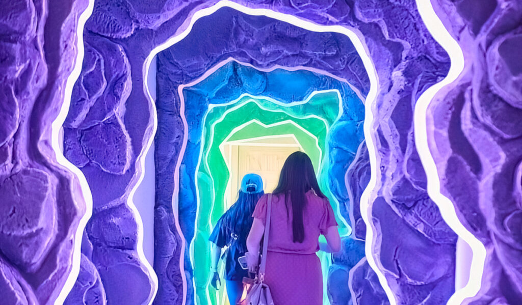 Two people walk along a purple and blue-lined hallway