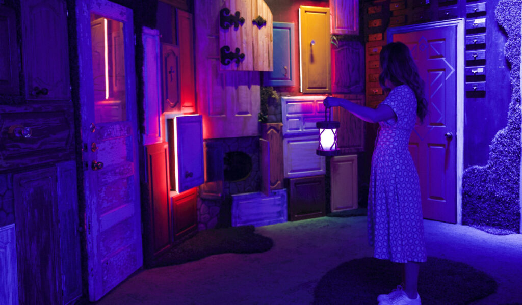 A woman holding a lantern stands before dozens of cabinet doors