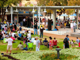 An outdoor park area with people sitting on blankets and walking around