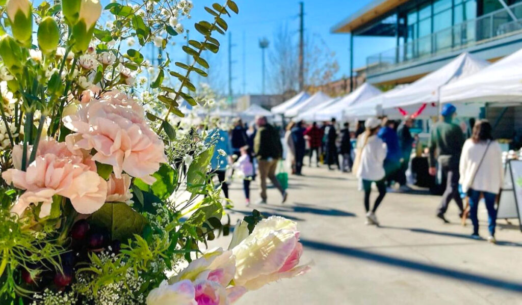 A close up of flowers with out-of-focus people shopping a market in the background