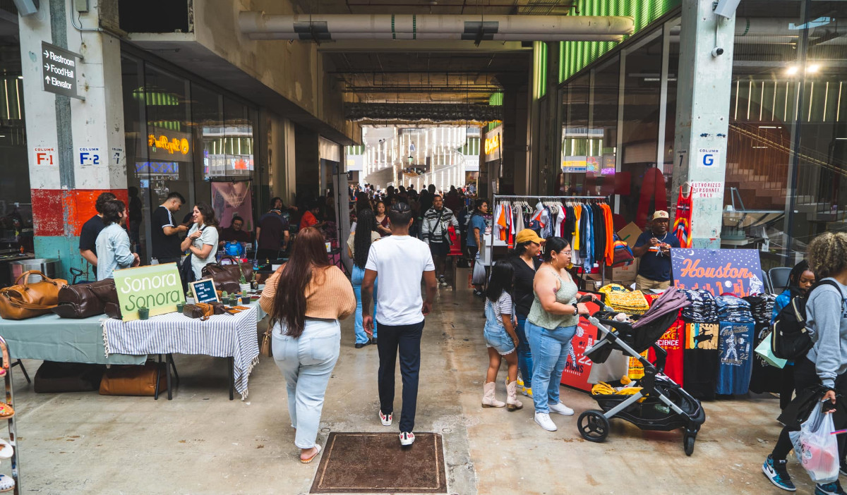 A bustling indoor market with vendors and people strolling past booths