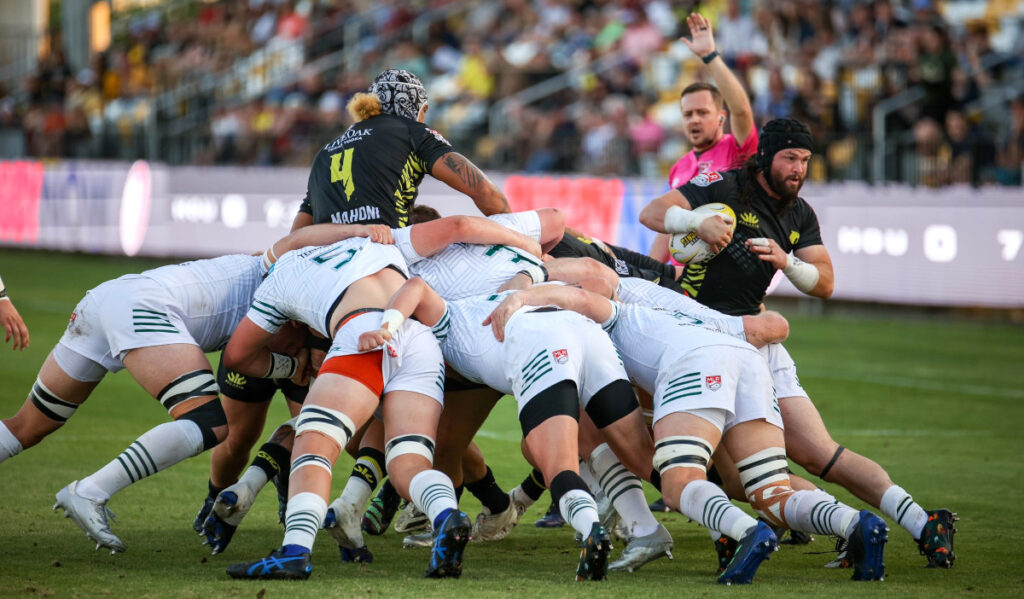 A rugby player emerges from a scrum with the ball