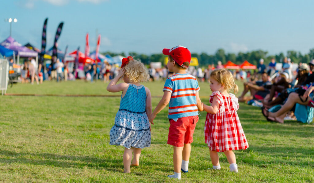 Three small children in red, white and blue clothes holding hands in a field