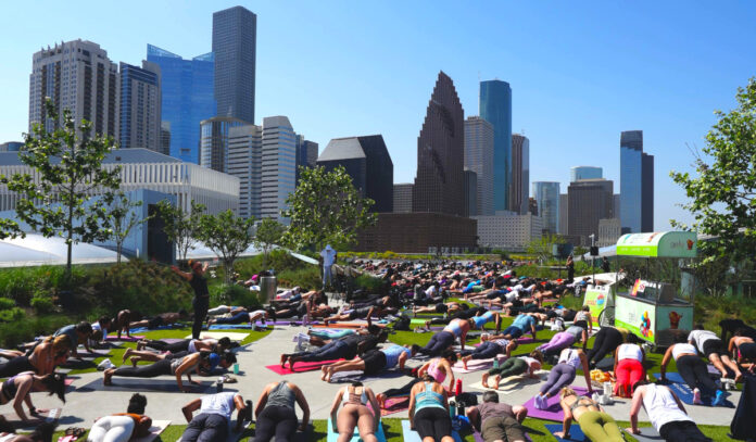 Dozens of people performing yoga postures on the Post Houston Skylawn