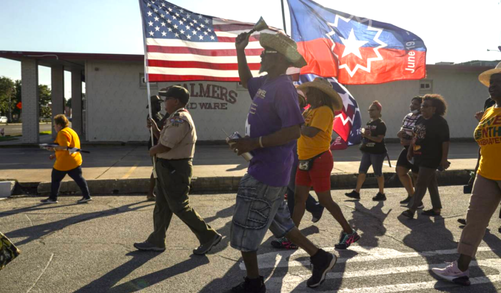 People walk through the streets with American and Juneteenth flags