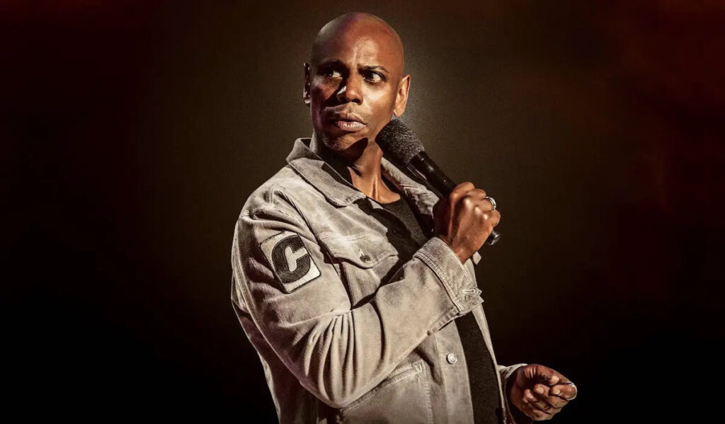 A promotional image of Dave Chappelle holding a microphone