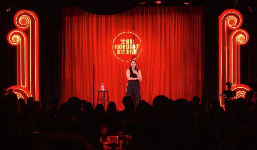 Comedian Kim Congdon performs in front of a red-draped stage