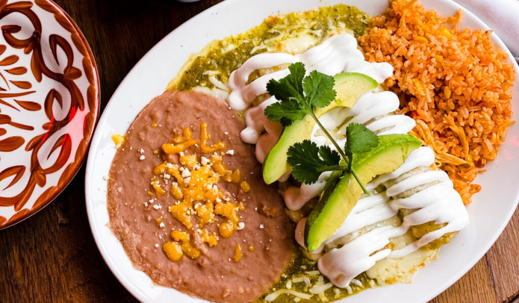 An overhead view of a plate of enchiladas with rice and beans