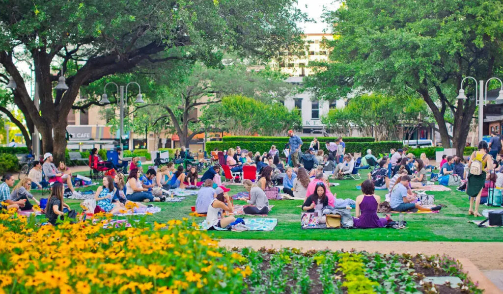 Groups of people sit on blankets across a bright green lawn