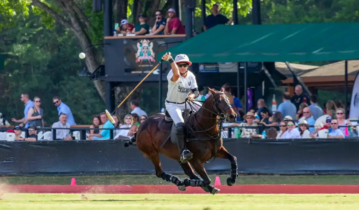 A polo player swings at the ball while riding a horse