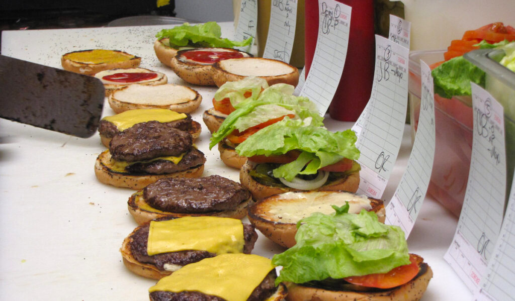 A line of burgers in the process of being prepared in a kitchen