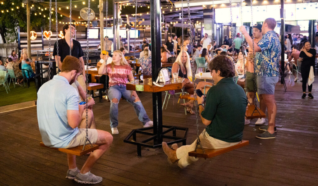 Bar patrons sit on swing seats and talk to each other