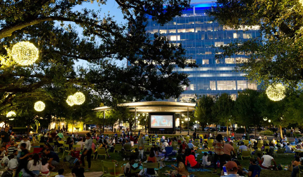 An evening movie screening at a public park with crowds of people in chairs and on blankets