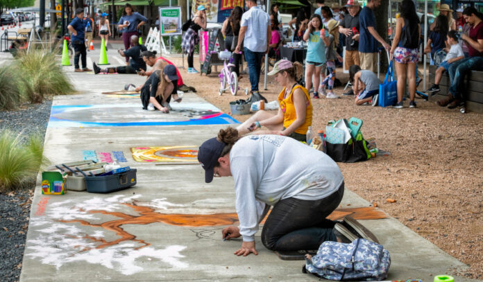 Artists kneel on the sidewalk to create chalk artwork