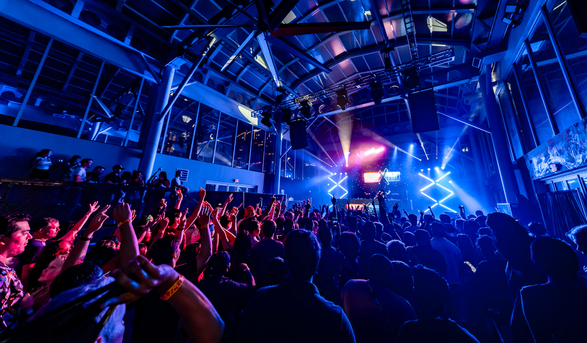 A blue-lit arena where crowds dance to DJs