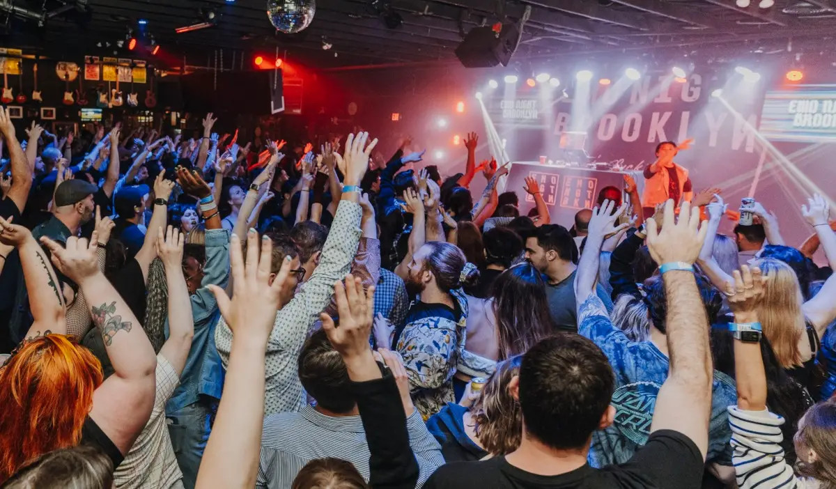 A crowd of people with hands in the air while DJs perform on stage