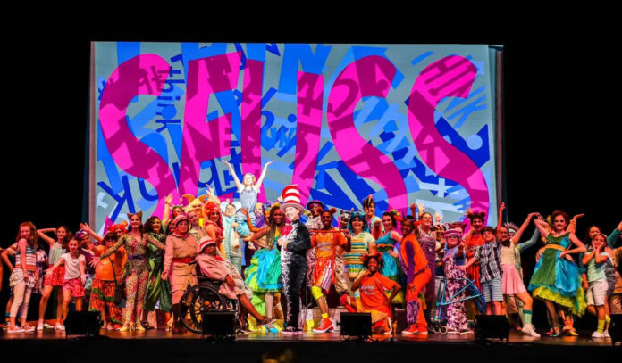 An ensemble cast posing in front of giant letters that spell "Seuss"