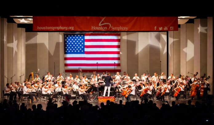 Houston Symphony performs on stage with an American flag behind them