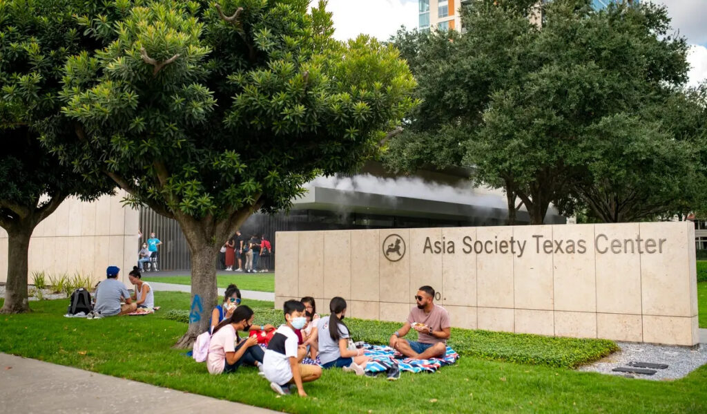 A family sits on a blanket outside of Asia Society Texas during a festival