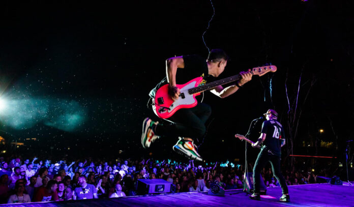 Mark Hoppus of Blink 182 leaps in the air while playing bass guitar