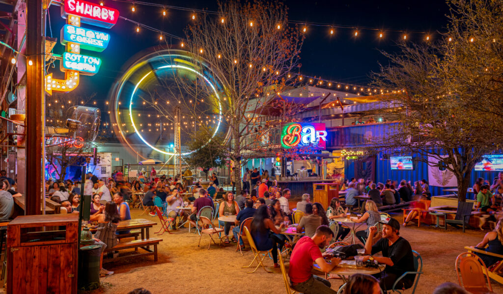 A night scene at an outdoor bar with bright neon lights and a Ferris Wheel