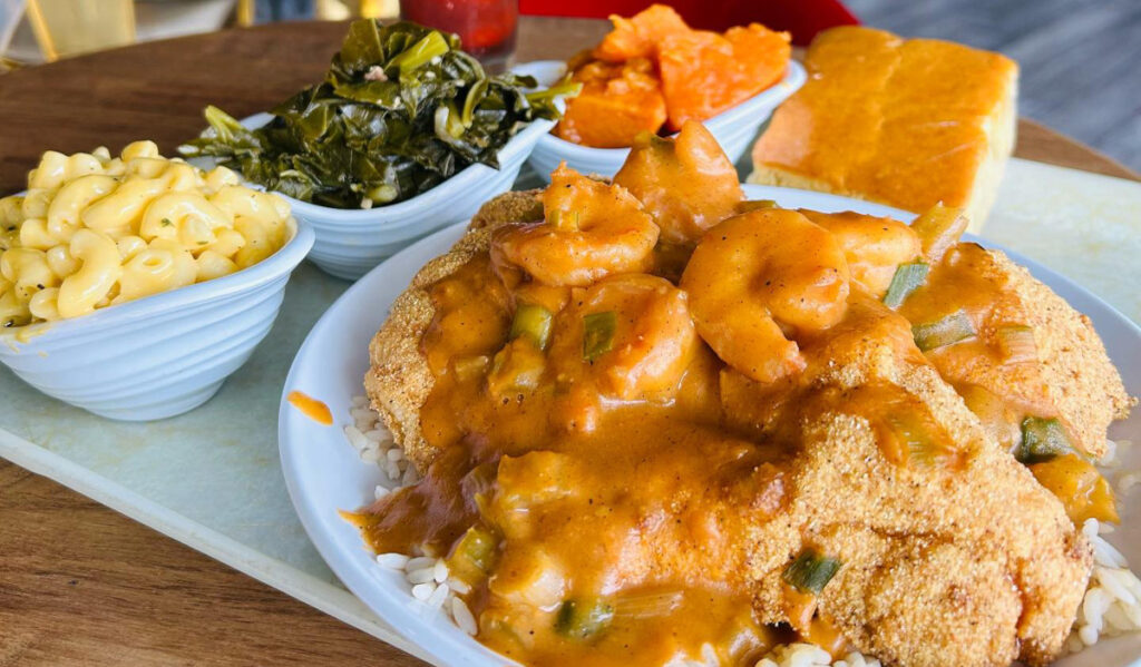 A plate of smothered fried catfish, with sides of collard greens and macaroni