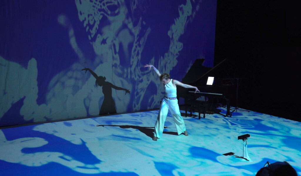 A dancer performs among blue swirling projections