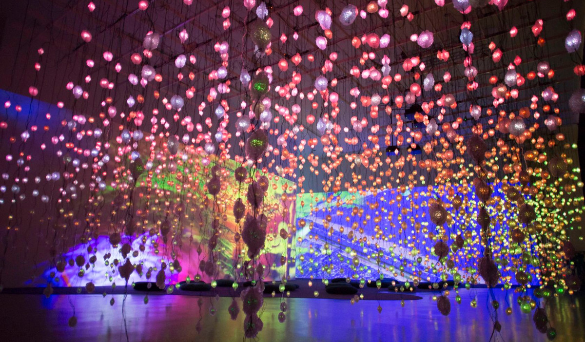 Strands of LED lights hang in the foreground with massive wall-sized projections in the background