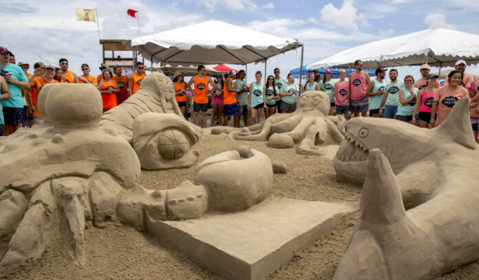 Teams line up around sandcastle sculptures of a shark, manatee, crab and octopus