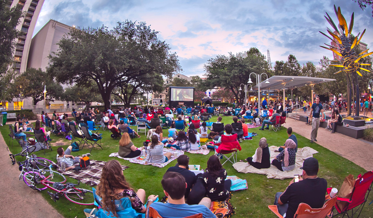 Groups of people sitting on blankets and in lawn chairs at Market Square Park, watching a movie