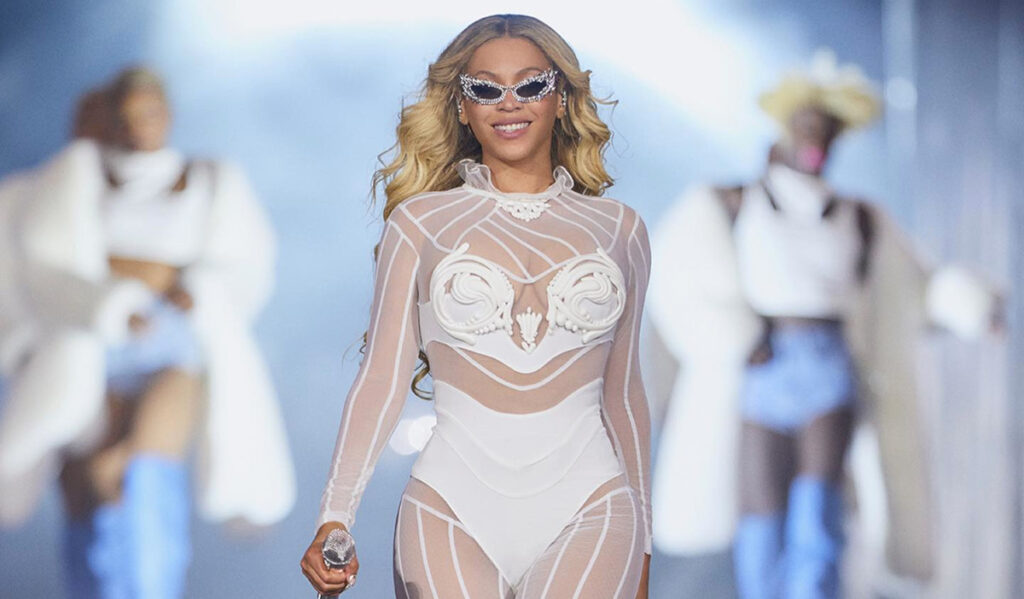 Beyoncé in a white costume and sunglasses smiling on stage