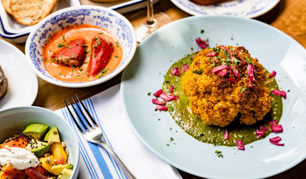 Three plates of dishes, including cauliflower, tomato and a salad