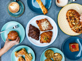 An overhead view of multiple plates of croissants, breads, and other brunch offerings