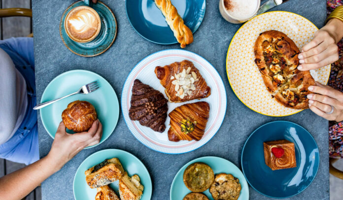 An overhead view of multiple plates of croissants, breads, and other brunch offerings