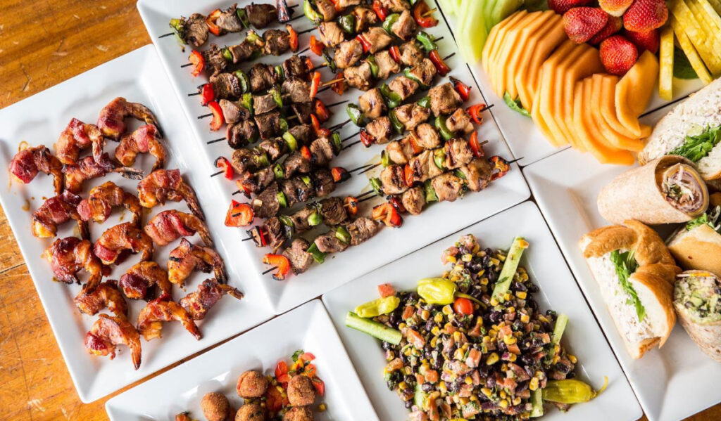 An overhead view of kabobs, fruit, salad and wraps