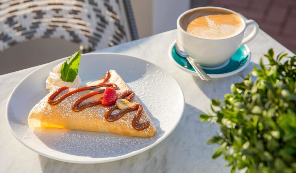 A sweet crepe with strawberry on top and a cup coffee on a sunny table