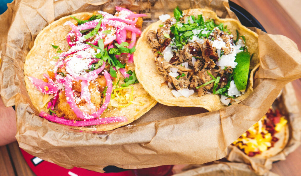Two open-faced tacos in a basket with meat, onion and cilantro