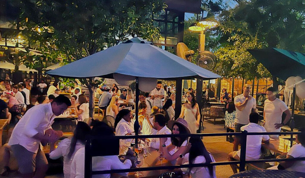 The patio of Heights Bier Garten at night with crowds of people dressed in white linen