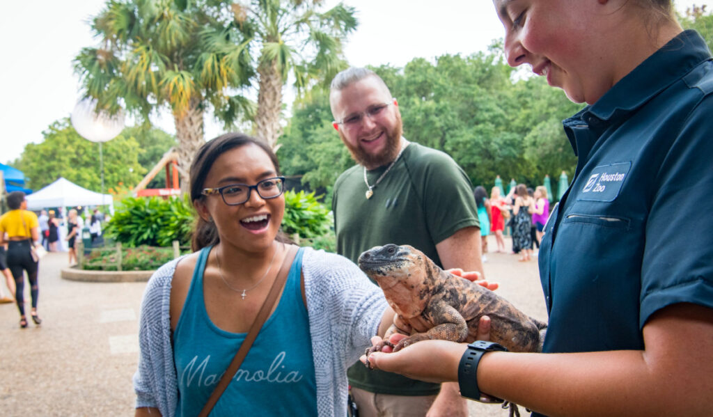 A person reaching out to touch a lizard held by a Houston Zoo staff member