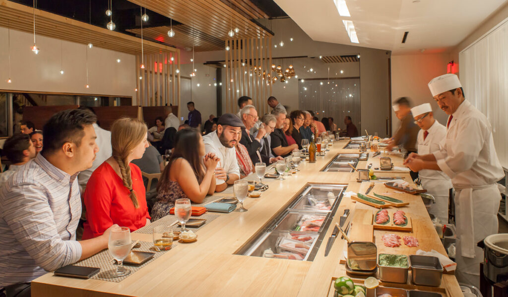 Patrons sit at an omakase counter as chefs prepare sushi