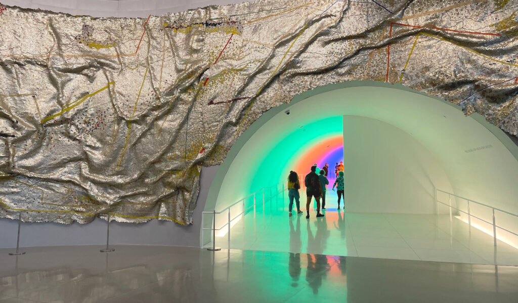 A small group of people walk through a colorful tunnel at MFAH
