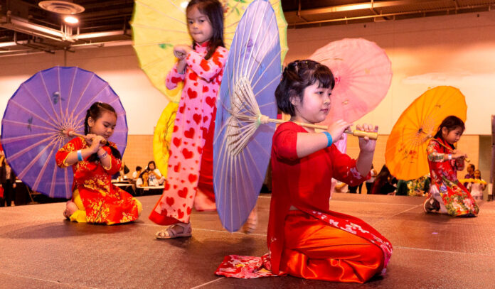 Children in traditional Vietnamese dress sit on a stage with umbrellas