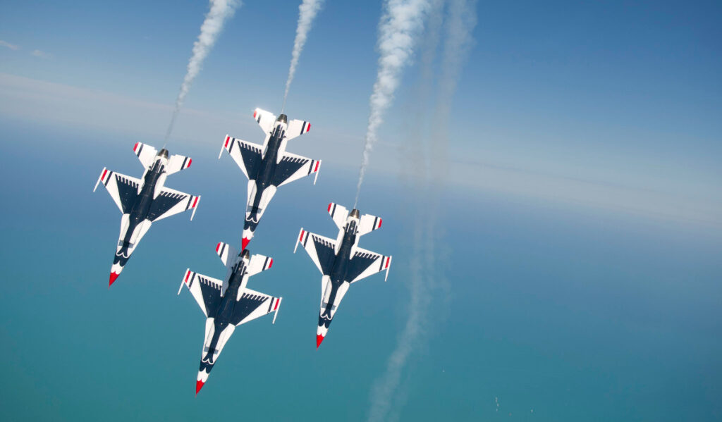 Four Air Force Thunderbirds fly overhead with trails behind them