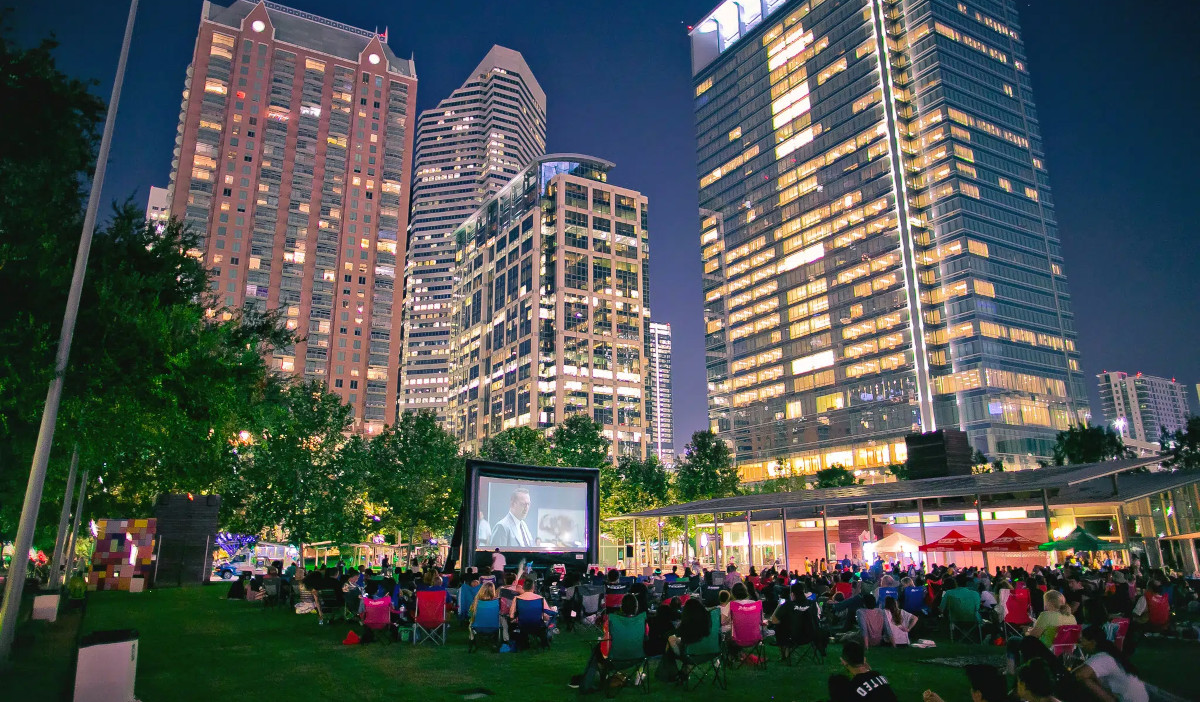 An outdoor movie screening at Discovery Green with towering skyscrapers behind the screen