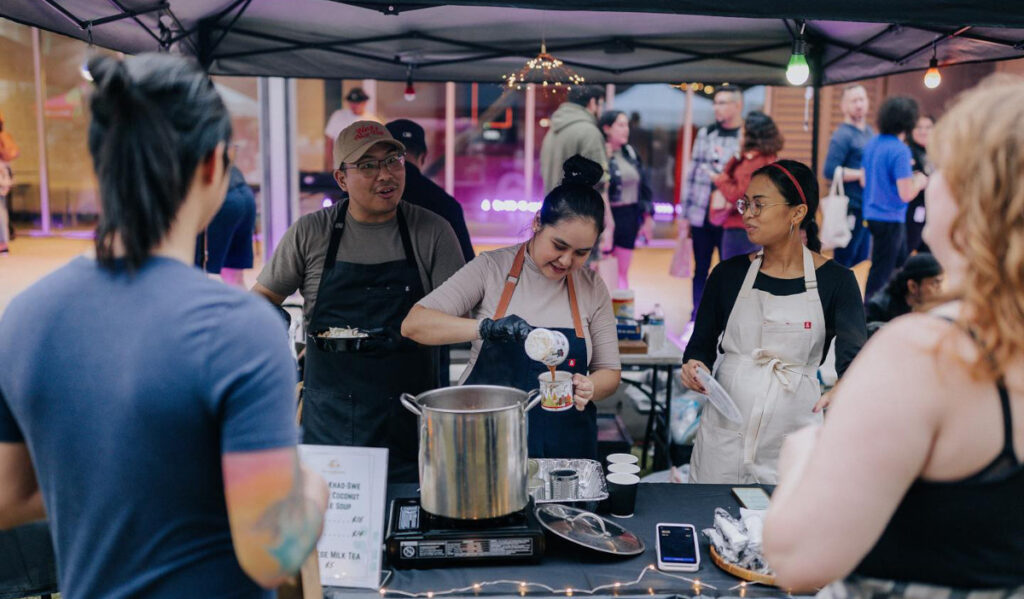 Three people serving drinks at a market stall