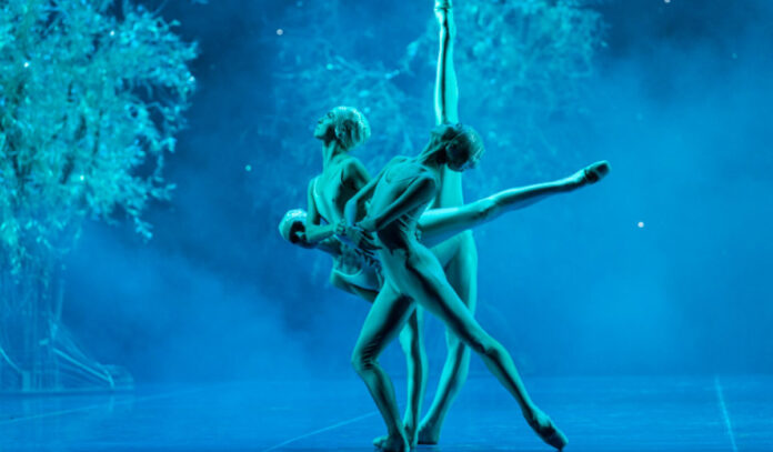 Three ballerinas pose while on a blue-lit stage