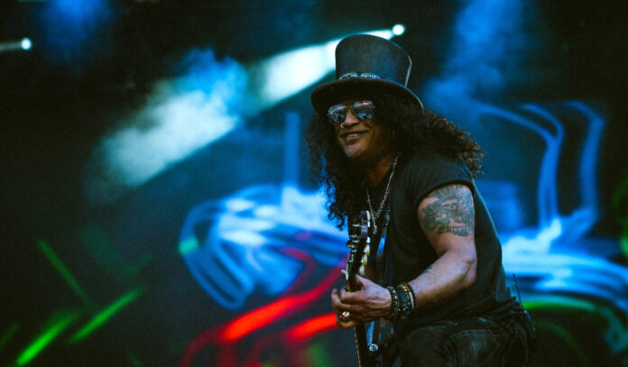 Guitarist Slash smiles while performing on stage